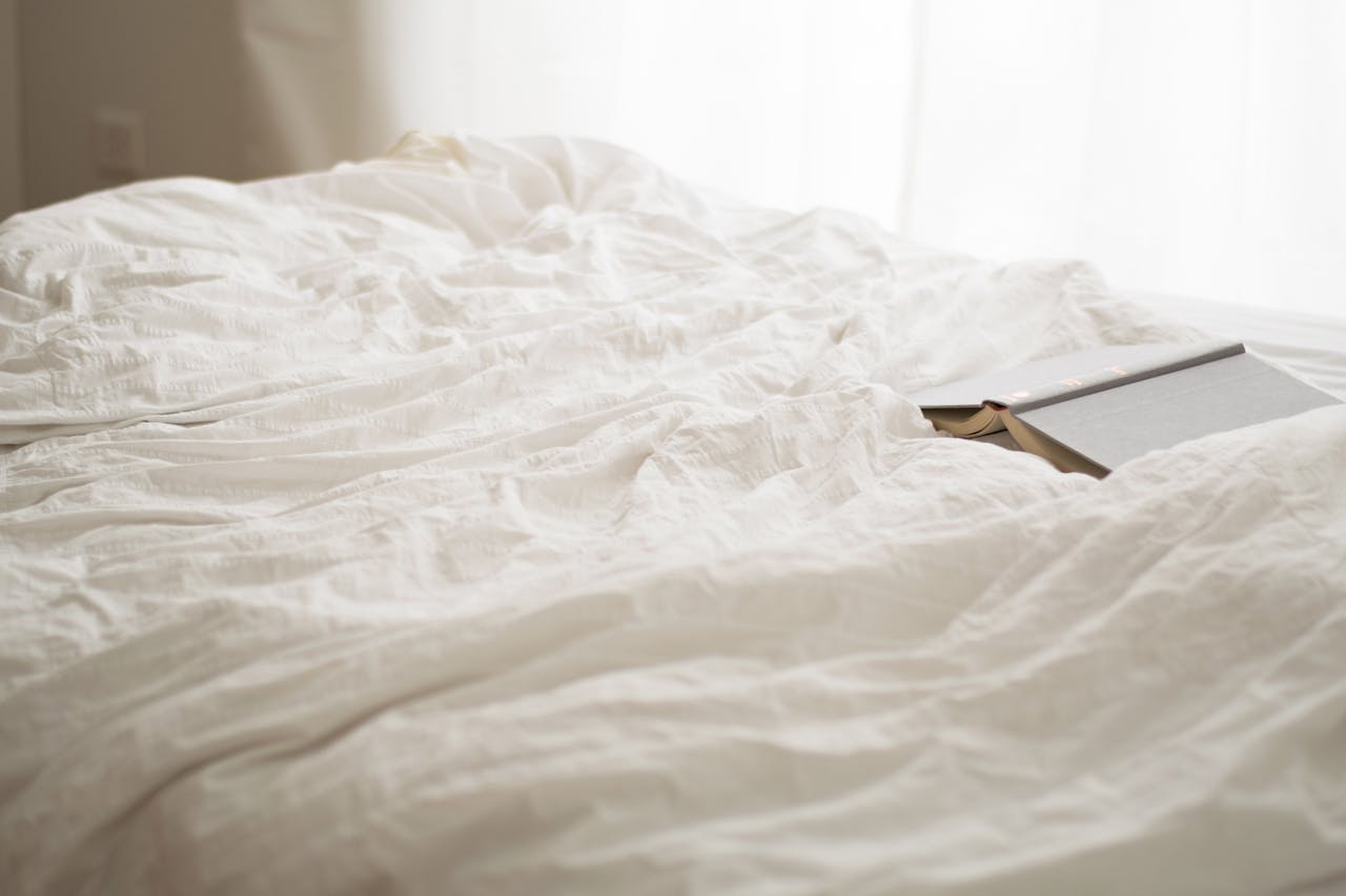 A serene bedroom scene with soft white sheets and a book, evoking relaxation and calm.